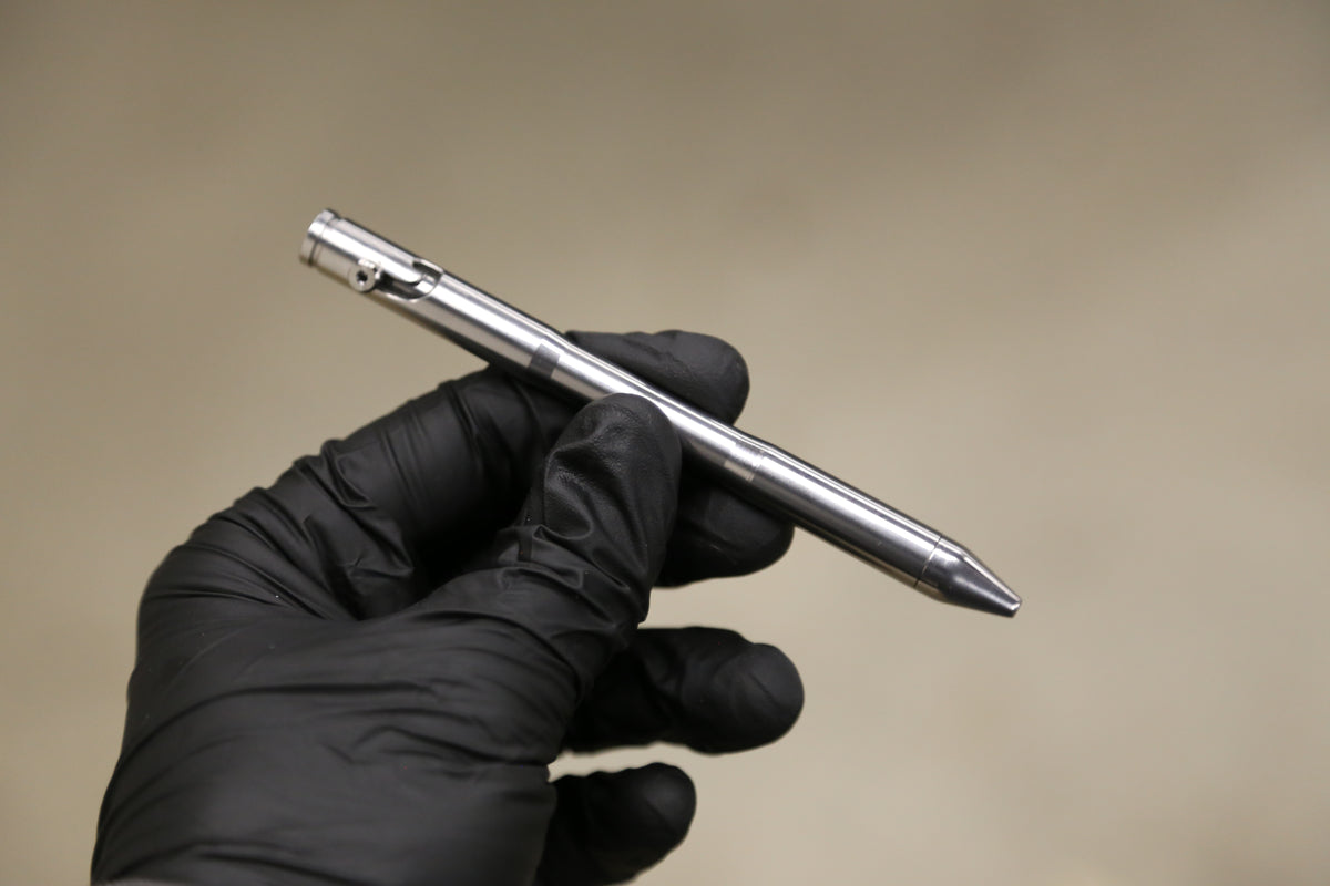 Drift titanium pen held in a black-gloved hand, showing its scale and machined finish.