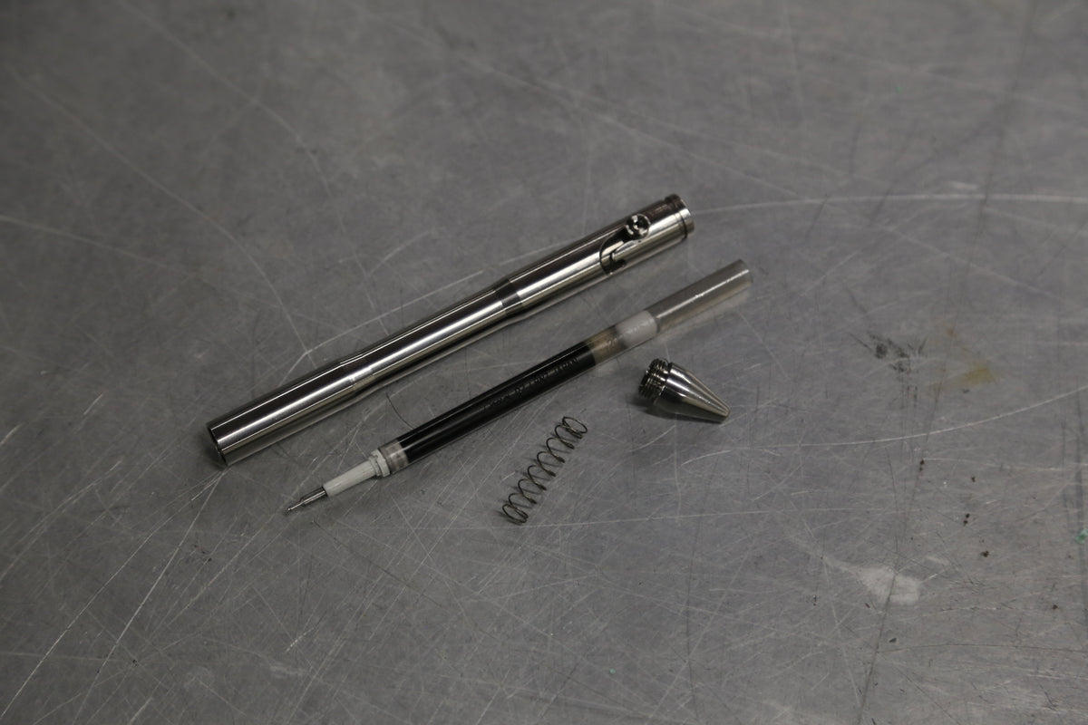 Drift pen body, refill, spring, and threaded tip laid out on a workbench.