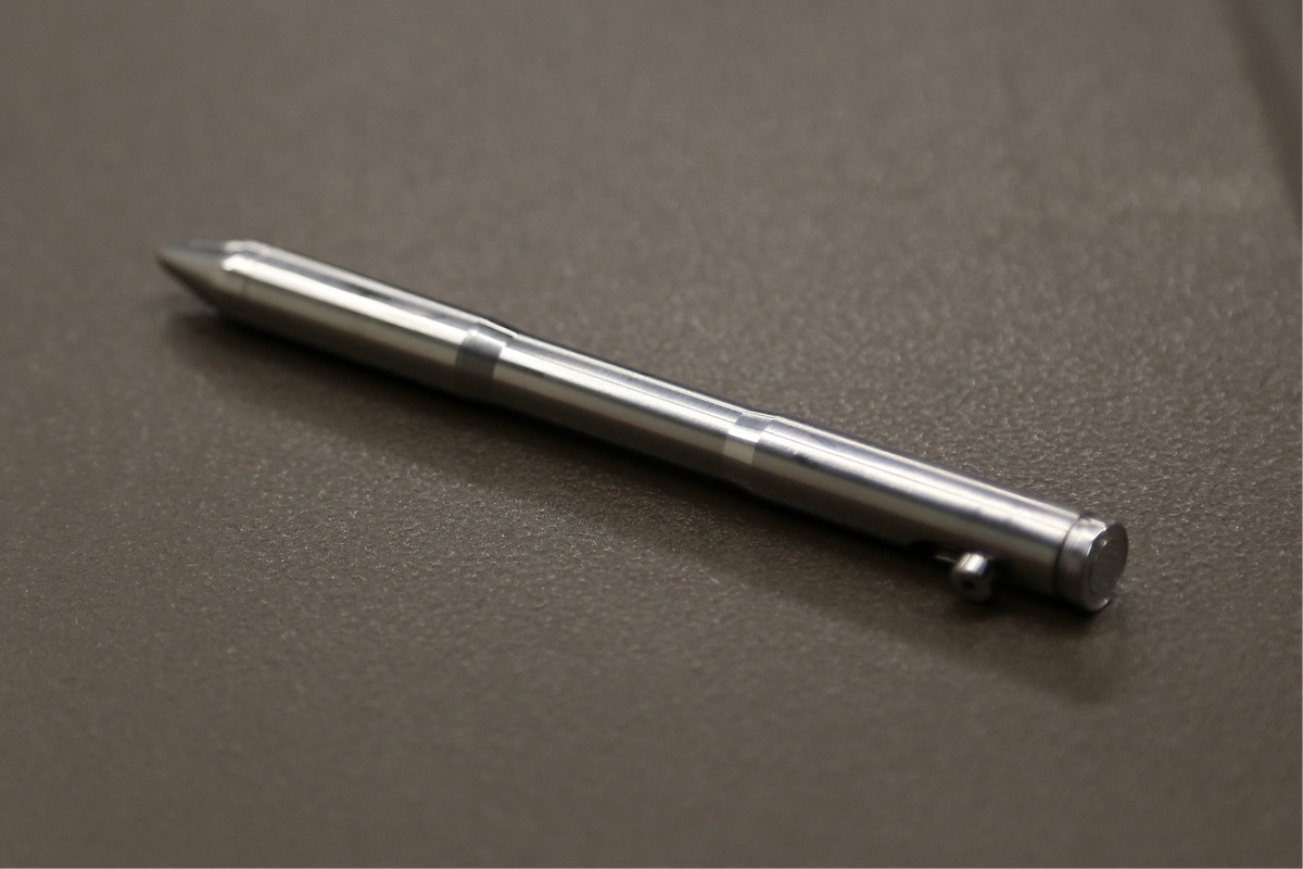 Raw machined Drift titanium bolt-action pen, closely framed on a workshop surface.